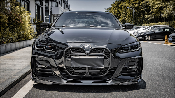 A sleek black car is parked on the side of a street, with modern headlights and a distinctive front grille. Buildings and parked cars line the background.