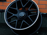 A black alloy wheel with a silver Mercedes emblem rests against a brick wall. 