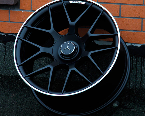 A black alloy wheel with a silver Mercedes emblem rests against a brick wall. "AMG" is inscribed at the top of the wheel rim, highlighting its premium design.