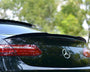A black Mercedes-Benz car is parked outdoors, its rear showcasing a sleek spoiler and distinctive taillights. The green background of trees suggests a serene, natural setting.
