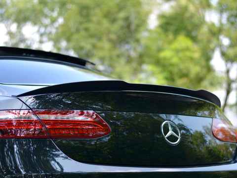 A black Mercedes-Benz car is parked outdoors, its rear showcasing a sleek spoiler and distinctive taillights. The green background of trees suggests a serene, natural setting.