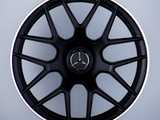 A black Mercedes-AMG wheel with a multi-spoke design stands upright against a gray background. The Mercedes logo is centered, with 