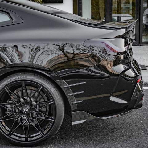 A sleek black sports car with intricate alloy wheels and sharp tail light design is parked outside a building. The tire displays the text "GOODYEAR."