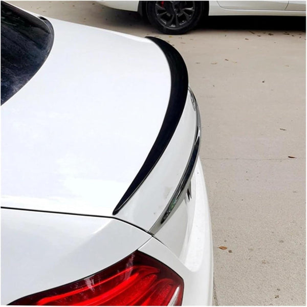 A white car with a black spoiler sits in a concrete parking area. Another car is partially visible in the background.