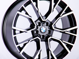 A sleek black and silver alloy wheel with a geometric design, centrally displaying the BMW logo, stands against a plain white background.