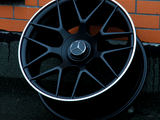 The black AMG-branded car wheel rests against an orange brick wall on a dark pavement. It features a Mercedes emblem in the center.