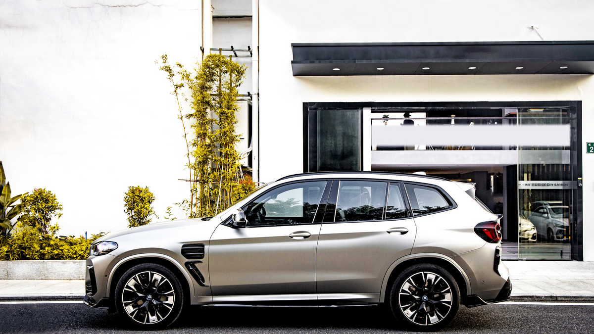 A sleek SUV is parked on a city street, adjacent to a modern building with large windows and labeled "INSTITUTE OF BY CARBON." Tall plants decorate the sidewalk.