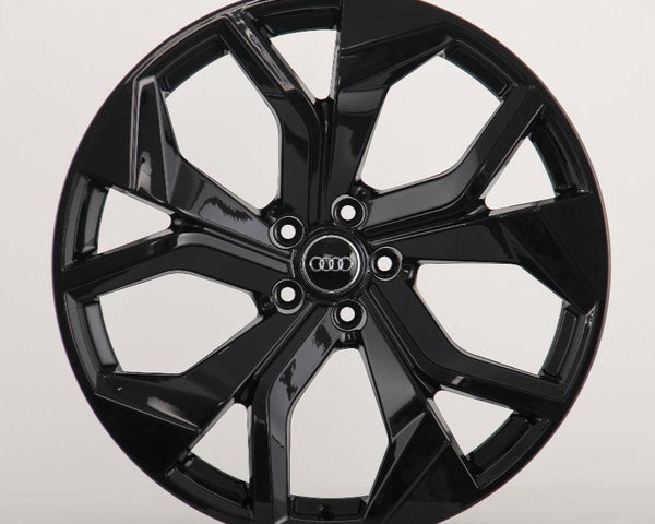 A black, glossy alloy wheel with a five-spoke design, displaying the Audi logo in the center, is positioned against a plain light gray background.