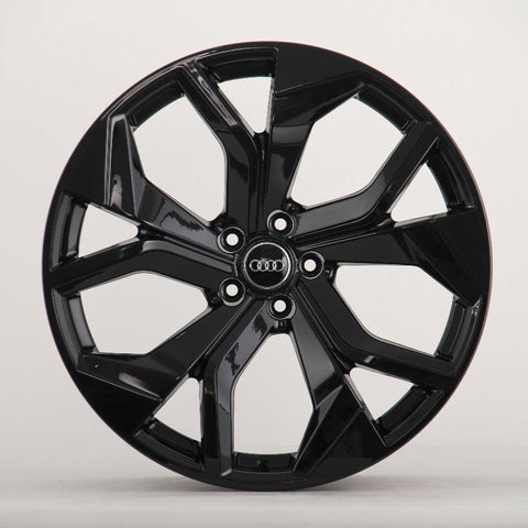 A black, glossy alloy wheel with a five-spoke design, displaying the Audi logo in the center, is positioned against a plain light gray background.