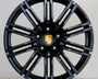 A black alloy wheel with multiple spokes features a central emblem displaying the Porsche logo. The wheel is positioned against a plain light gray background.