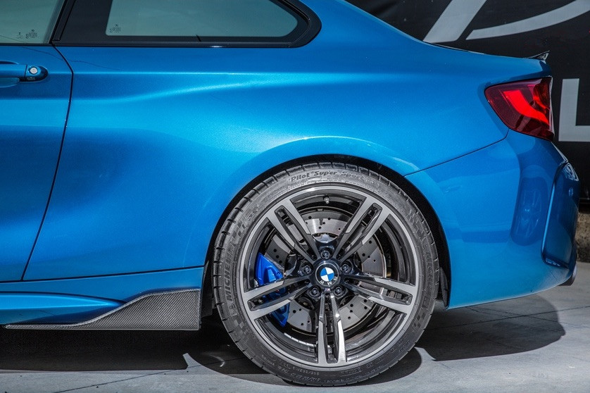 A blue car, focusing on its rear quarter panel and wheel, is parked on a concrete surface. The tire reads "Pilot Super Sport," and the brake caliper is painted blue.