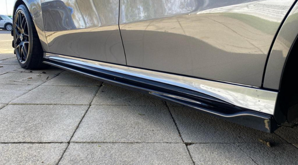 A sleek car with black side skirts is parked on a tiled surface, with another vehicle visible in the distant background.