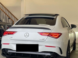 A white Mercedes-Benz AMG CLA 45 S is parked in a garage, illuminated by indoor lighting. It features quad exhausts, tinted windows, and visible branding. Text: 