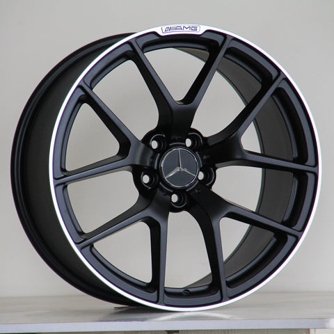 A black alloy wheel with a Mercedes-Benz logo is resting on a wooden surface against a plain background. Text on the rim reads "AMG" with a stylized logo.