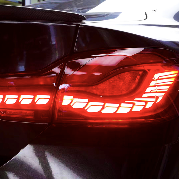 A car's taillight is illuminated in bright red, showing a sleek, modern design with horizontal light strips, set against a glossy black car exterior.