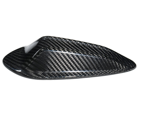 A carbon fiber cover with a sleek, aerodynamic shape sits isolated against a plain white background, highlighting its glossy weave pattern.