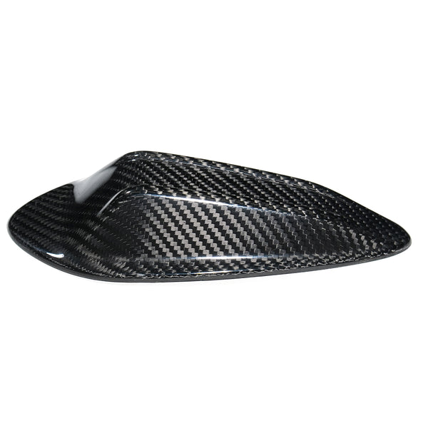 A carbon fiber cover with a sleek, aerodynamic shape sits isolated against a plain white background, highlighting its glossy weave pattern.