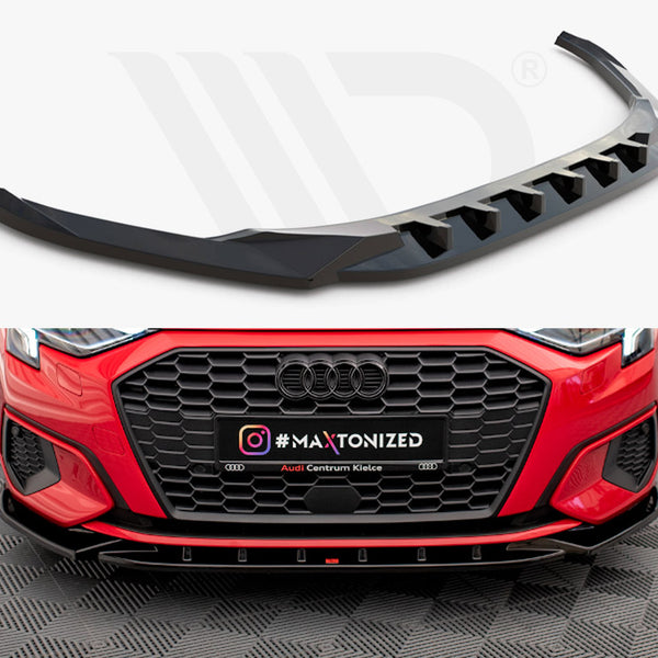 A black car front splitter, designed for aerodynamics, is showcased above a red Audi with a black grille. Below, text reads "#MAXTONIZED" and "Audi Centrum Kielce" on a patterned floor.