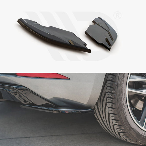 Two black aerodynamic car parts are shown above a rear view of a car. The car's rear diffuser and tire are visible on a concrete surface.