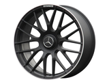 A black, multi-spoke car wheel rim features a Mercedes logo at its center, with 