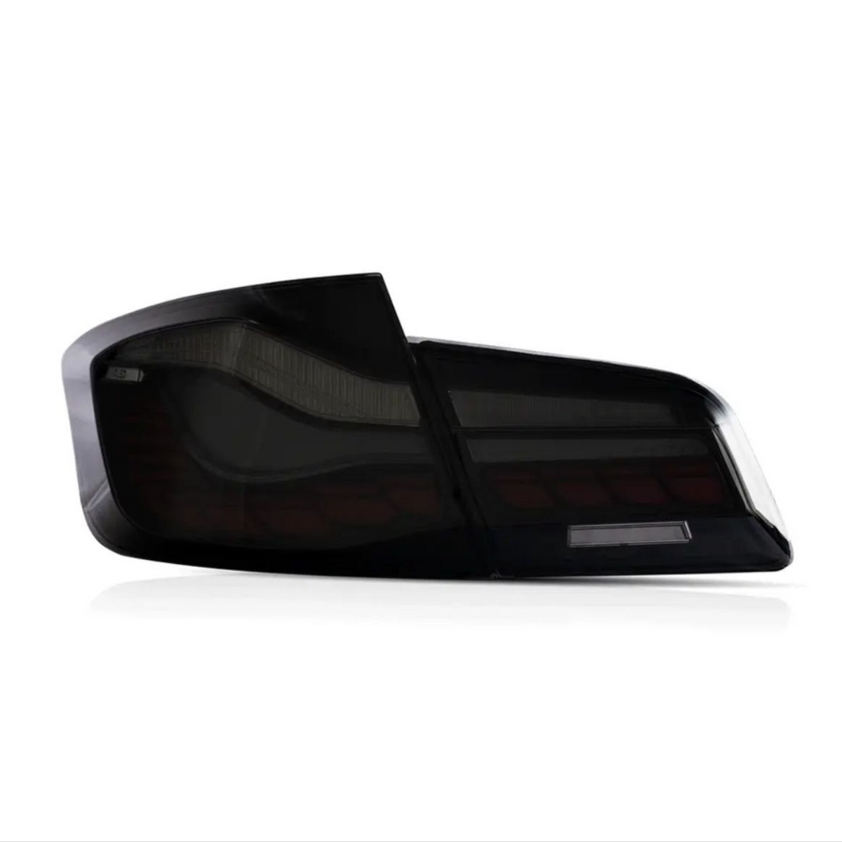 A sleek, dark tail light with a modern design sits against a plain white background, highlighting its reflective and angular features.