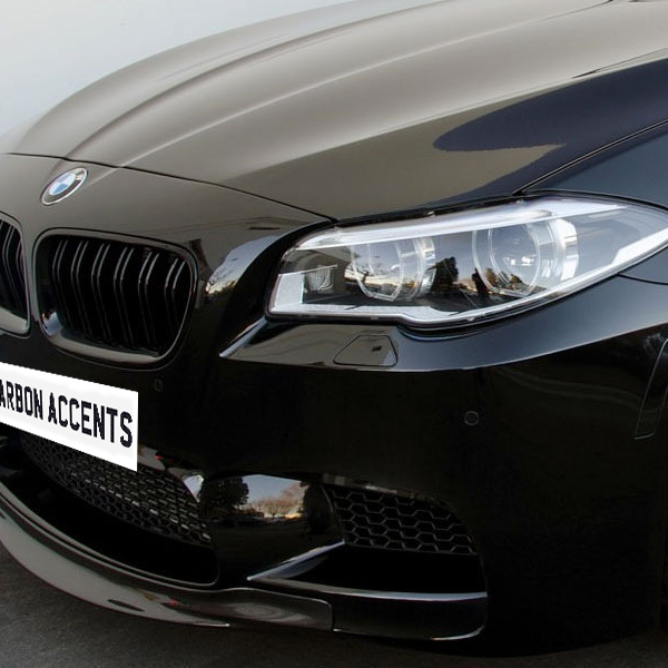 Black car with a sleek front design and shiny headlight, parked on a concrete surface. The license plate area displays the text "CARBON ACCENTS."