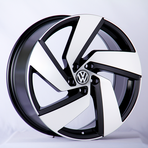 A car wheel rim displays a black-and-white geometric spoke design with a Volkswagen logo at the center, set against a plain white background.