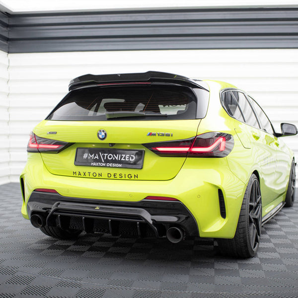 A bright yellow BMW M135i is parked in a white, enclosed garage. The license plate reads "#MAXTONIZED, MAXTON DESIGN", and the car features a sporty rear diffuser and black wheels.