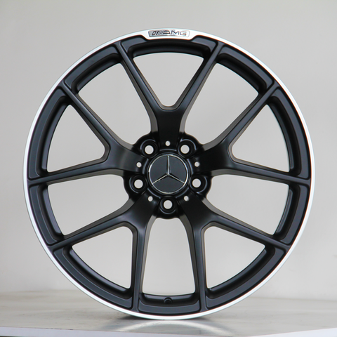 A black alloy wheel with a Mercedes logo in the center and "AMG" label on the rim, resting on a light-colored surface against a plain background.