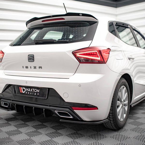 White hatchback car, stationary, in a modern showroom with a geometric wall design. The rear features the words "IBIZA" and a "Maxton Design" bumper detail.