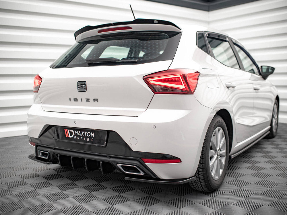 White hatchback car, stationary, in a modern showroom with a geometric wall design. The rear features the words "IBIZA" and a "Maxton Design" bumper detail.