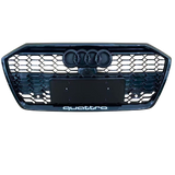 A front car grille displays the Audi logo with four rings and a honeycomb pattern. Below, "quattro" text is located. The background is plain, emphasizing the grille design.