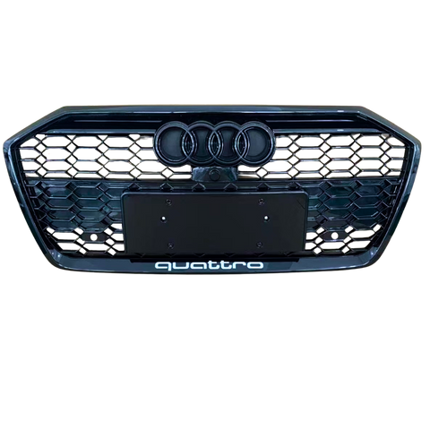 A front car grille displays the Audi logo with four rings and a honeycomb pattern. Below, "quattro" text is located. The background is plain, emphasizing the grille design.
