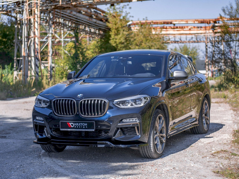 A black BMW SUV is parked on a gravel path, with metal scaffolding and green foliage in the background. The license plate reads "MAXTON design."