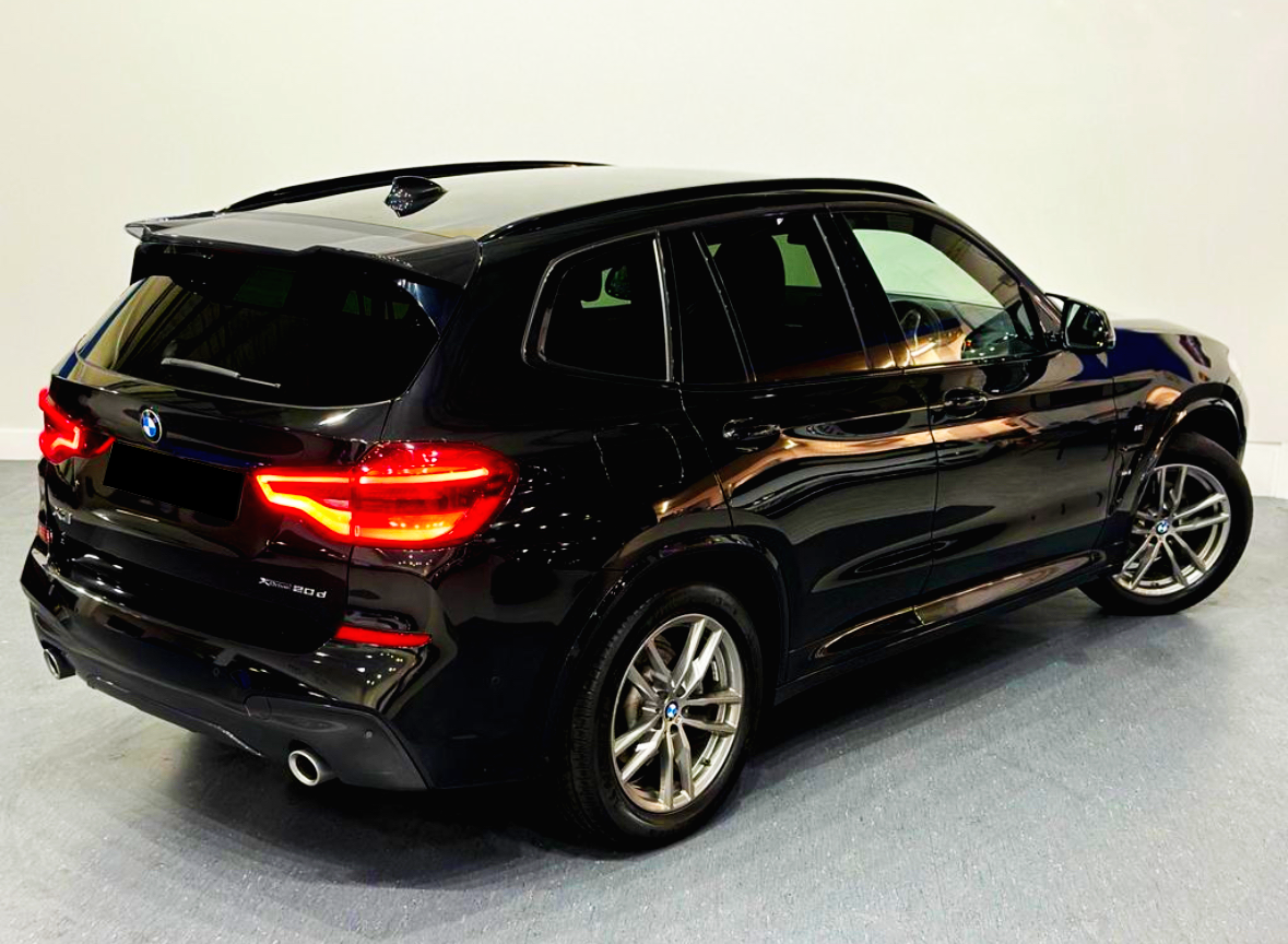 A black BMW X3 SUV stands parked in a brightly lit room. The car's rear lights are illuminated, highlighting its sleek design.