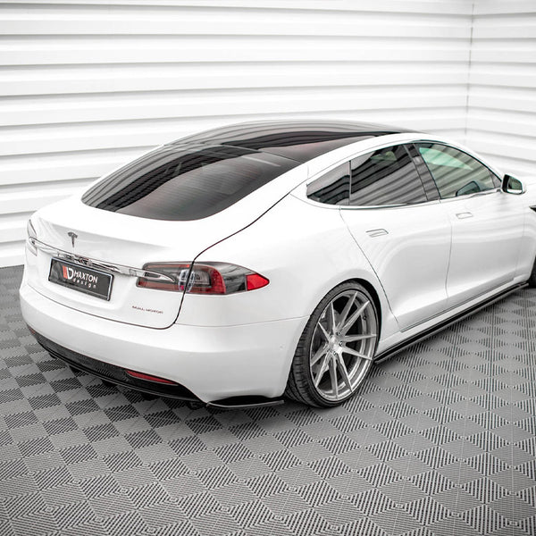 A white car is parked, showcasing large alloy wheels, in a patterned, enclosed setting. A sign on the rear reads "Maxton Design."