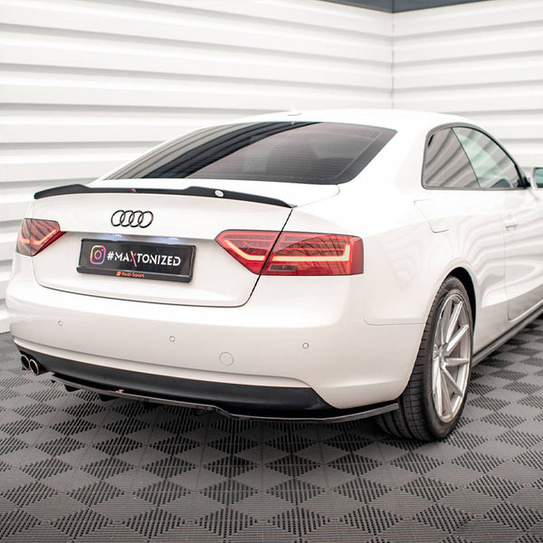 A white car is parked in a corner of a room with patterned flooring. The license plate reads "#MAATONIZED." The car is an Audi, surrounded by white, textured walls.