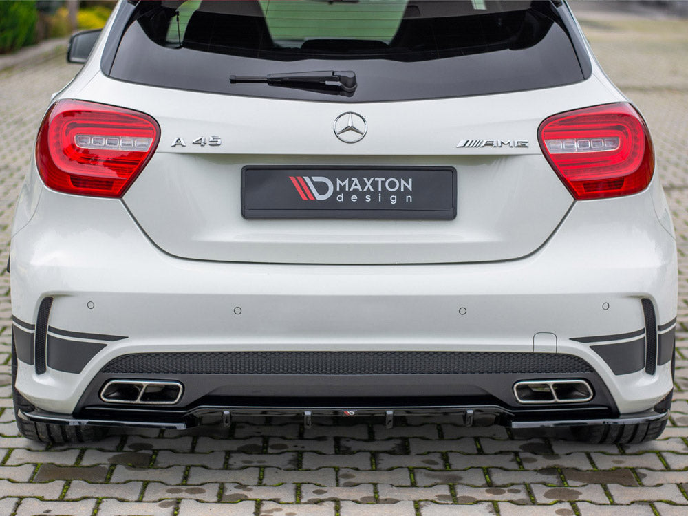 A white Mercedes A 45 AMG car is parked on a cobblestone surface, featuring a Maxton Design rear bumper and dual exhaust outlets.