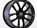 A black alloy wheel with ten sleek spokes displays a Tesla logo at the center. It rests on a plain white background, showcasing its glossy finish and intricate design.