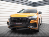 A gold-colored Audi SUV is parked on a checkered floor inside a showroom. The front grille features a prominent Audi logo. The license plate reads: 