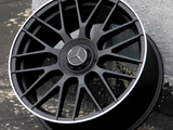 A black alloy wheel with a three-pointed star emblem rests against a textured wall. Text on the wheel reads 