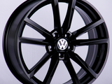 A glossy black alloy wheel featuring the Volkswagen logo at its center, positioned upright against a plain, light gray background.