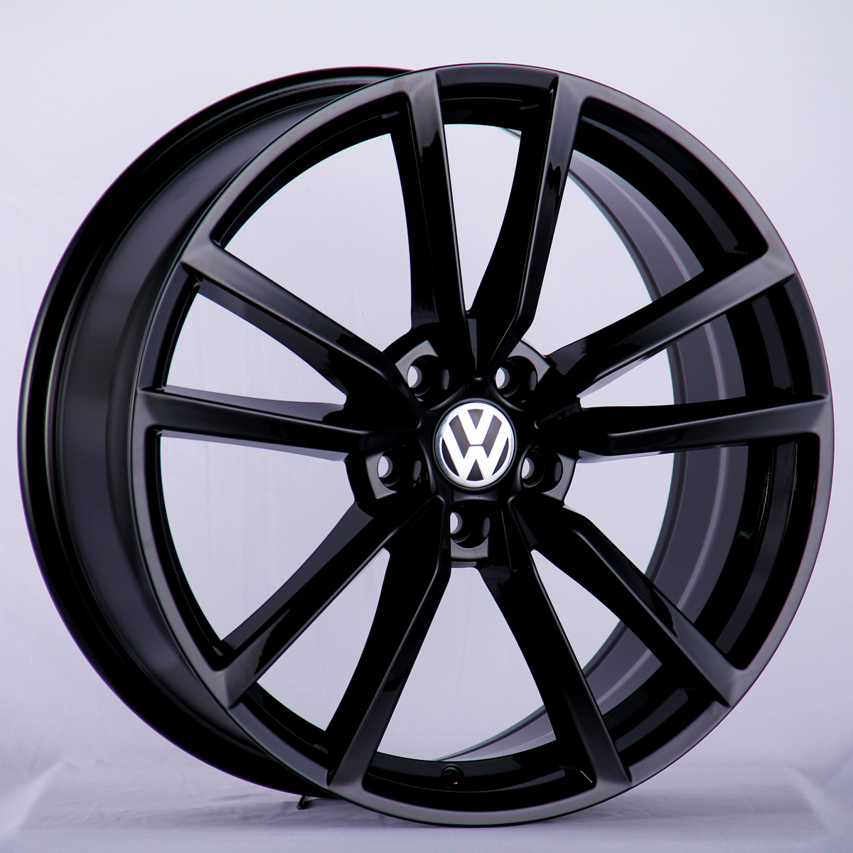 A glossy black alloy wheel featuring the Volkswagen logo at its center, positioned upright against a plain, light gray background.