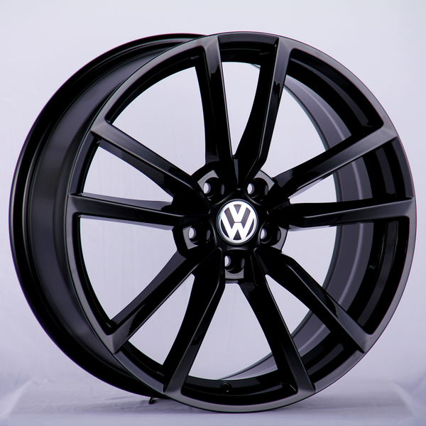 A glossy black alloy wheel featuring the Volkswagen logo at its center, positioned upright against a plain, light gray background.