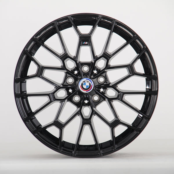 A black multi-spoke alloy wheel is displayed upright, featuring a BMW emblem in the center. The intricate design sits against a plain, light gray backdrop.