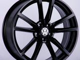 A black alloy wheel with a multi-spoke design displays the Volkswagen logo at the center, presented against a plain, light background.