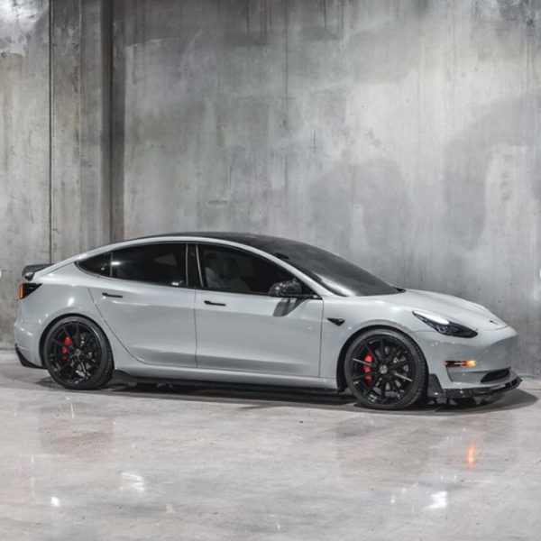 A sleek, gray sedan is parked on a shiny concrete floor, with black wheels and red brake calipers, set against an industrial, textured gray wall.