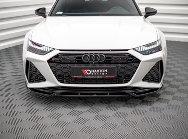 A white Audi car is stationary with its front visible, detailed with a prominent black grille and LED headlights. It is set in a white, patterned studio. Text: "MAXTON DESIGN."