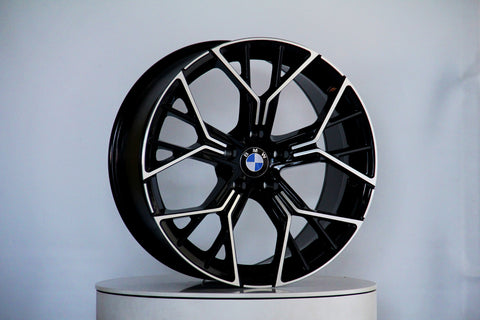 A black and silver alloy wheel with a BMW logo in the center is displayed on a circular platform against a plain light gray background.