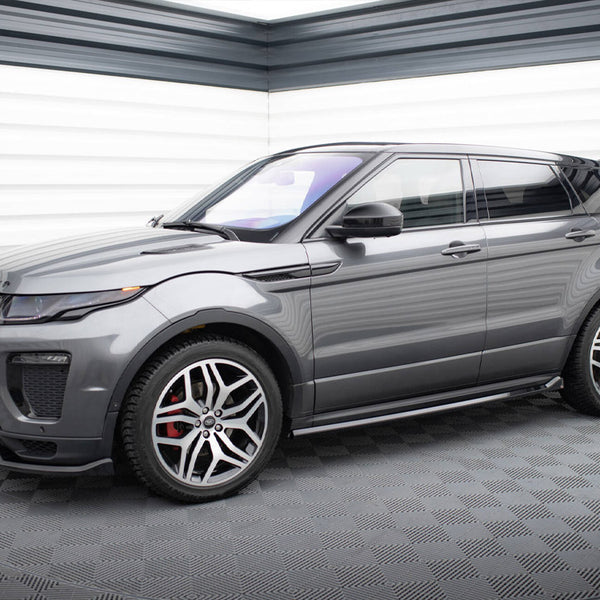 A sleek gray SUV with sporty rims is parked indoors on a textured floor, surrounded by striped white and gray paneled walls. The front displays "RANGE ROVER" on the hood.